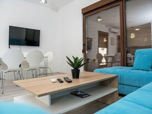 Una sala de estar moderna con una mesa de centro de madera, una planta en maceta, un sofá azul y un televisor de pantalla plana montado en la pared.