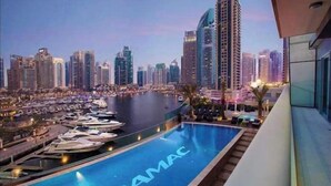 Una piscina con la marca 'DAMAC', un puerto deportivo con barcos y un paisaje urbano con rascacielos al fondo.
