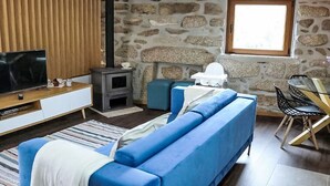 A living room with a stone wall, a television, a sofa, a chair, and a fireplace. - Ruhe, einzigartiger Raum! by Interhome (Aguiar da Beira)