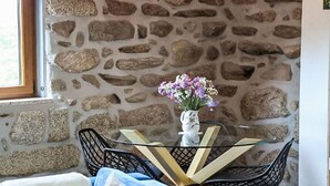 A stone wall, a glass table with chairs, and a vase with flowers. - Ruhe, einzigartiger Raum! by Interhome (Aguiar da Beira)