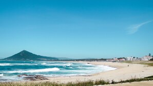 A beach with waves, a mountain, and buildings in the distance. - Wohnung "Juste Au" über dem Meer by Interhome (Caminha)