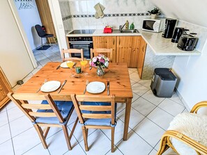 Un comedor con una mesa y sillas de madera, una cocina con microondas y cafetera, y un cubo de basura.