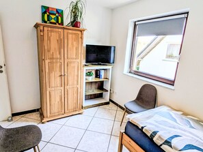 Una habitación con un armario de madera, televisión, cama, silla y ventana con vista a una escalera.
