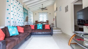 A living room with a sectional sofa, a glass coffee table, a ceiling fan, and a TV. - Gemütlicher karibischer Rückzugsort gegenüber dem Strand by Interhome (Sandy Lane)
