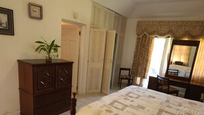 Een slaapkamer met een bed, een kaptafel, een stoel, een spiegel en een deur naar een andere kamer.