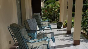 Een overdekt terras met metalen stoelen en een betegelde vloer.