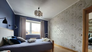 Ein Schlafzimmer mit einem Bett, einem Nachttisch, einem Fenster mit Vorhängen, einer Chandelüster und einem Holzboden.