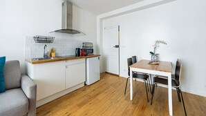 Una cocina compacta con armarios blancos, una encimera de madera, horno empotrado y refrigerador pequeño. Hay una mesa de comedor con sillas y un florero con flores.