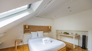 Un dormitorio moderno con techo inclinado, cabecero de madera, mesita de noche, escritorio y radiador.