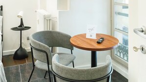 A small, modern room with a round wooden table and two grey chairs. A small black lamp is on a side table, and a remote control is on the table. A sign indicating wifi is visible. - Turin Central Carlo Felice (Turin)