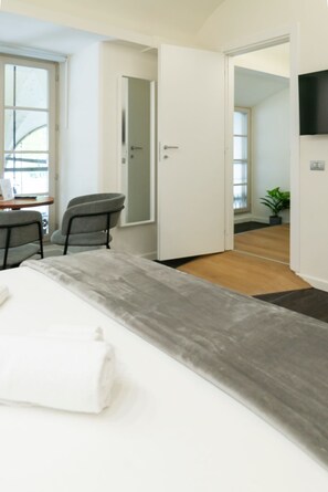 A modern hotel room with a bed, a desk, and a chair. There is a door leading to another room and a plant in the corner. - Turin Central Carlo Felice (Turin)