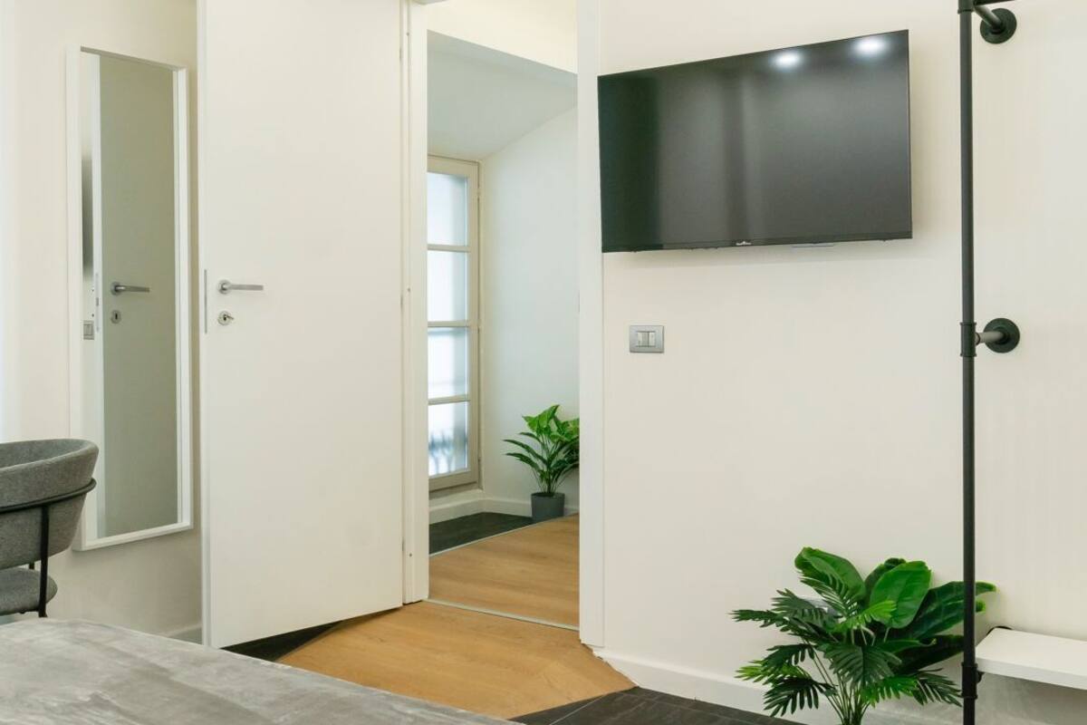 Ein modernes Schlafzimmer mit einem Bett, einem an der Wand montierten Fernseher und einer Tür zu einem anderen Raum.