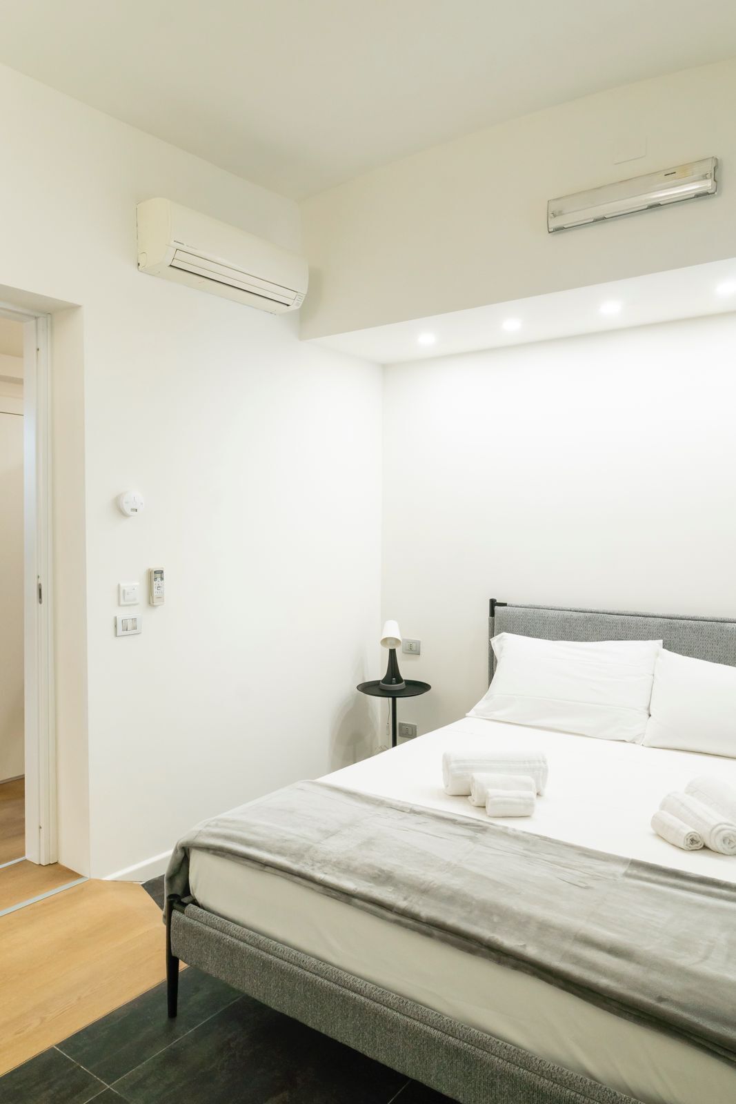 Ein ordentlich eingerichtetes Schlafzimmer mit einem Bett, einer Nachttischlampe und einer Wand-Klimaanlage.