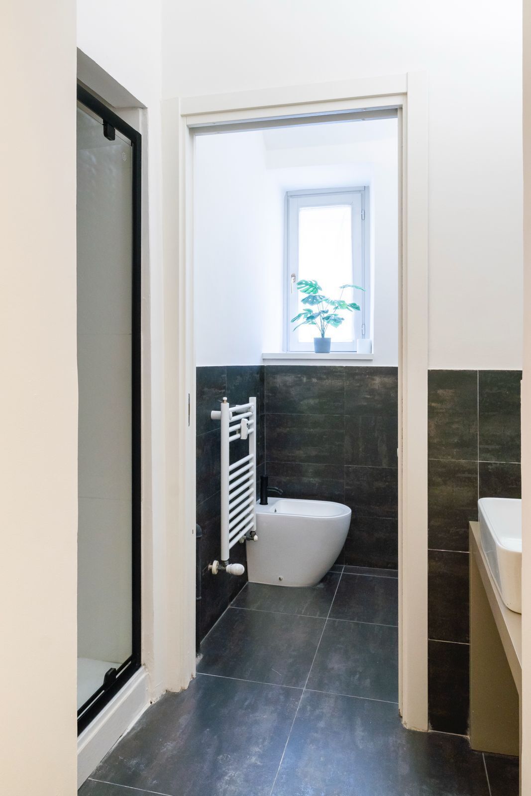 Ein modernes Badezimmer mit Dusche, Bidet und einem kleinen Fenster mit Pflanze.