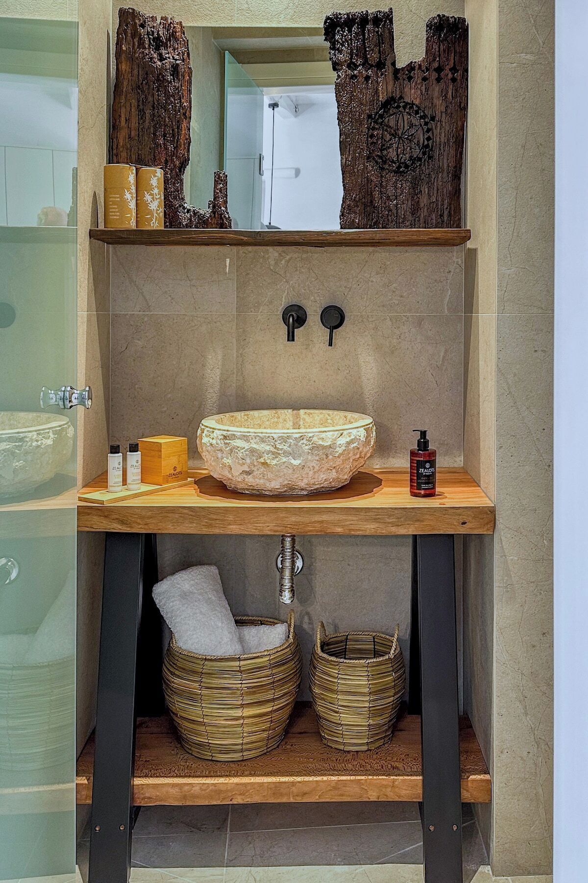 Un baño con un lavamanos de piedra, estantes de madera y cestas tejidas.