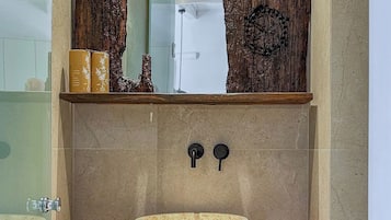 Un baño con un lavamanos de piedra, estantes de madera y cestas tejidas.