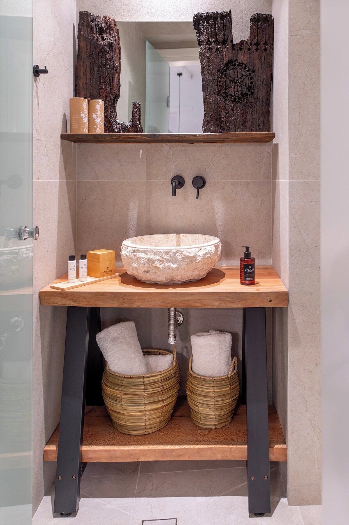 Une salle de bain avec un lavabo en pierre, des étagères en bois et des paniers en osier.