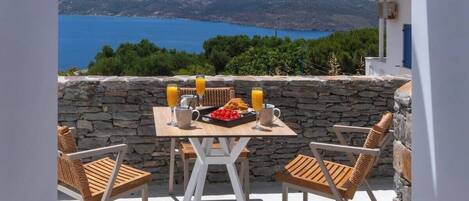 A terrace with a table set for breakfast, overlooking a coastal landscape.