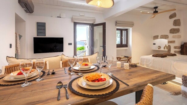 Un comedor con una mesa de madera dispuesta para dos personas, un televisor y una pared de piedra.