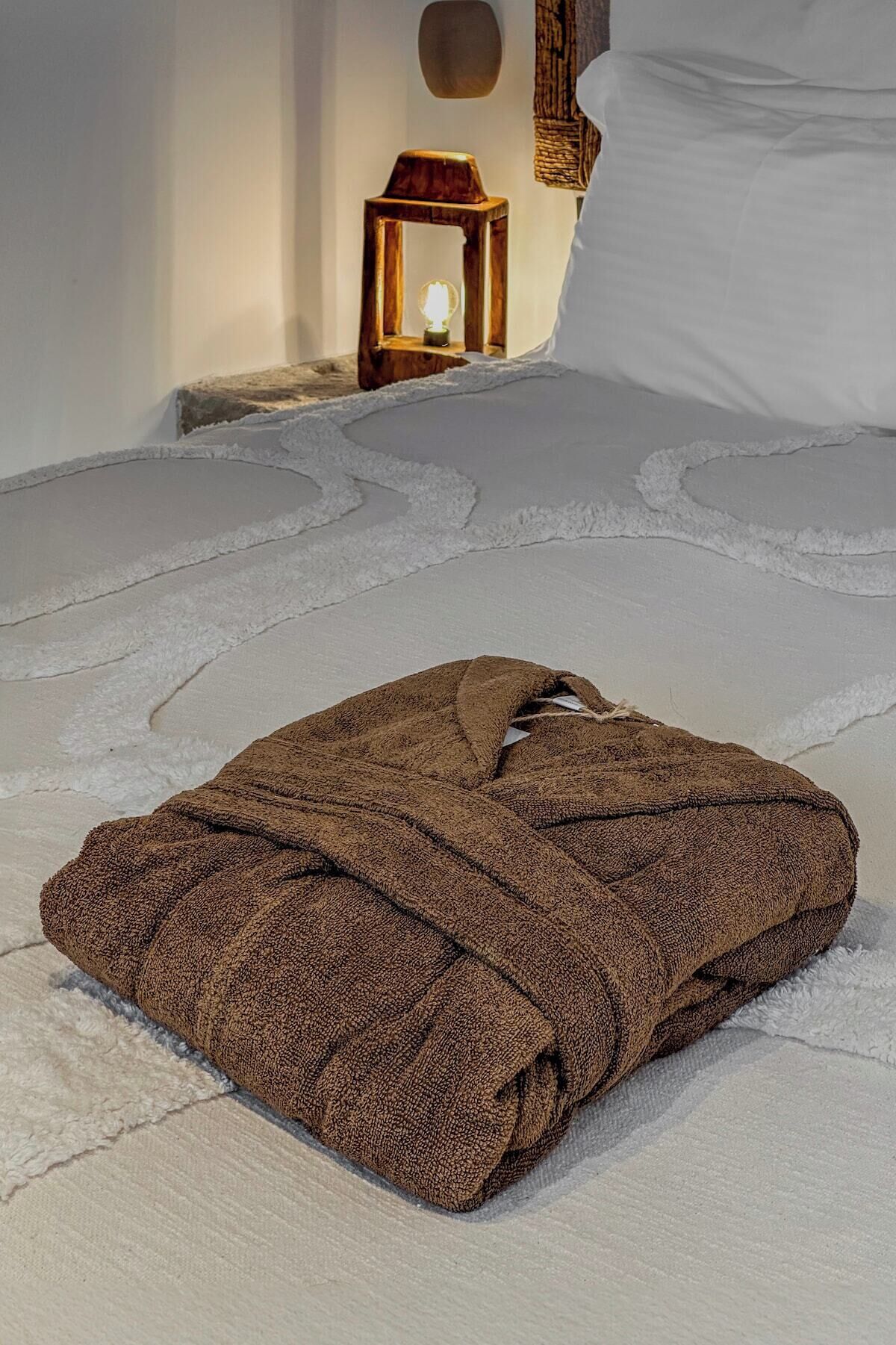 Una manta marrón doblada con cuidado sobre una cama de textura blanca y suave.