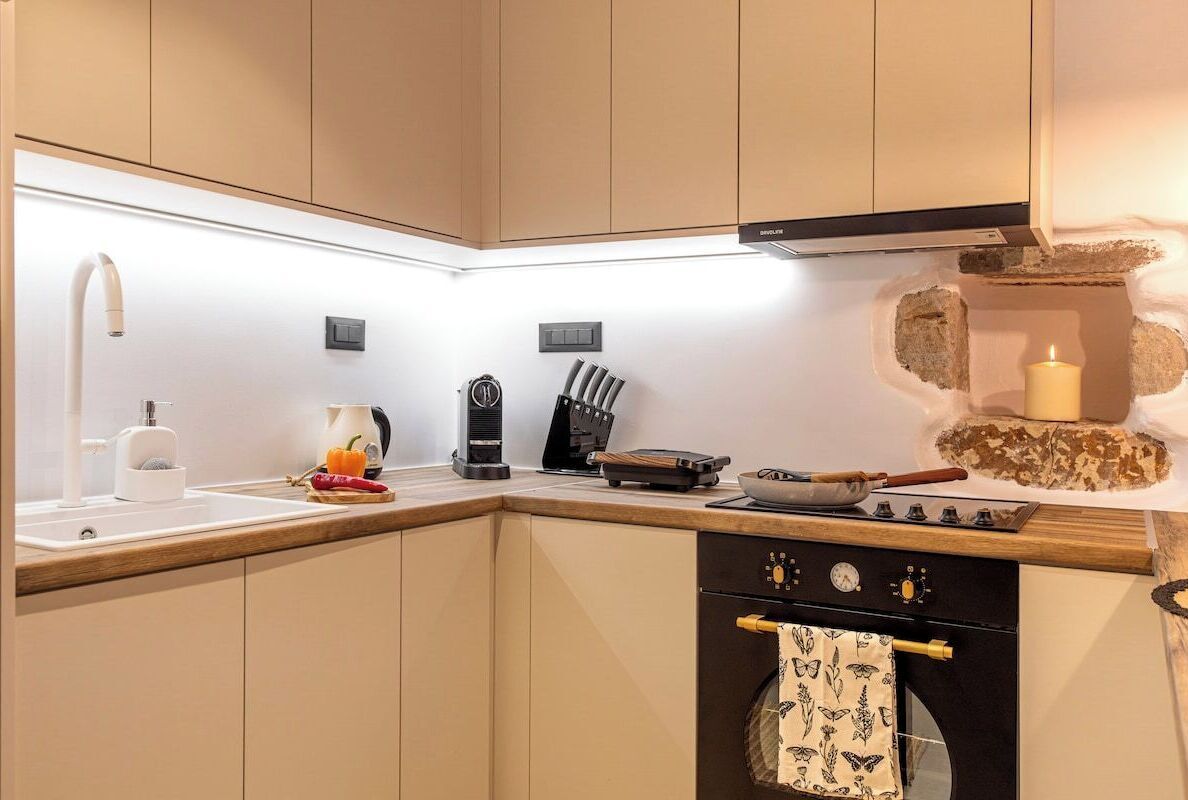 A compact kitchen with a sink, stove, and oven, featuring wooden cabinets and a tiled backsplash.
