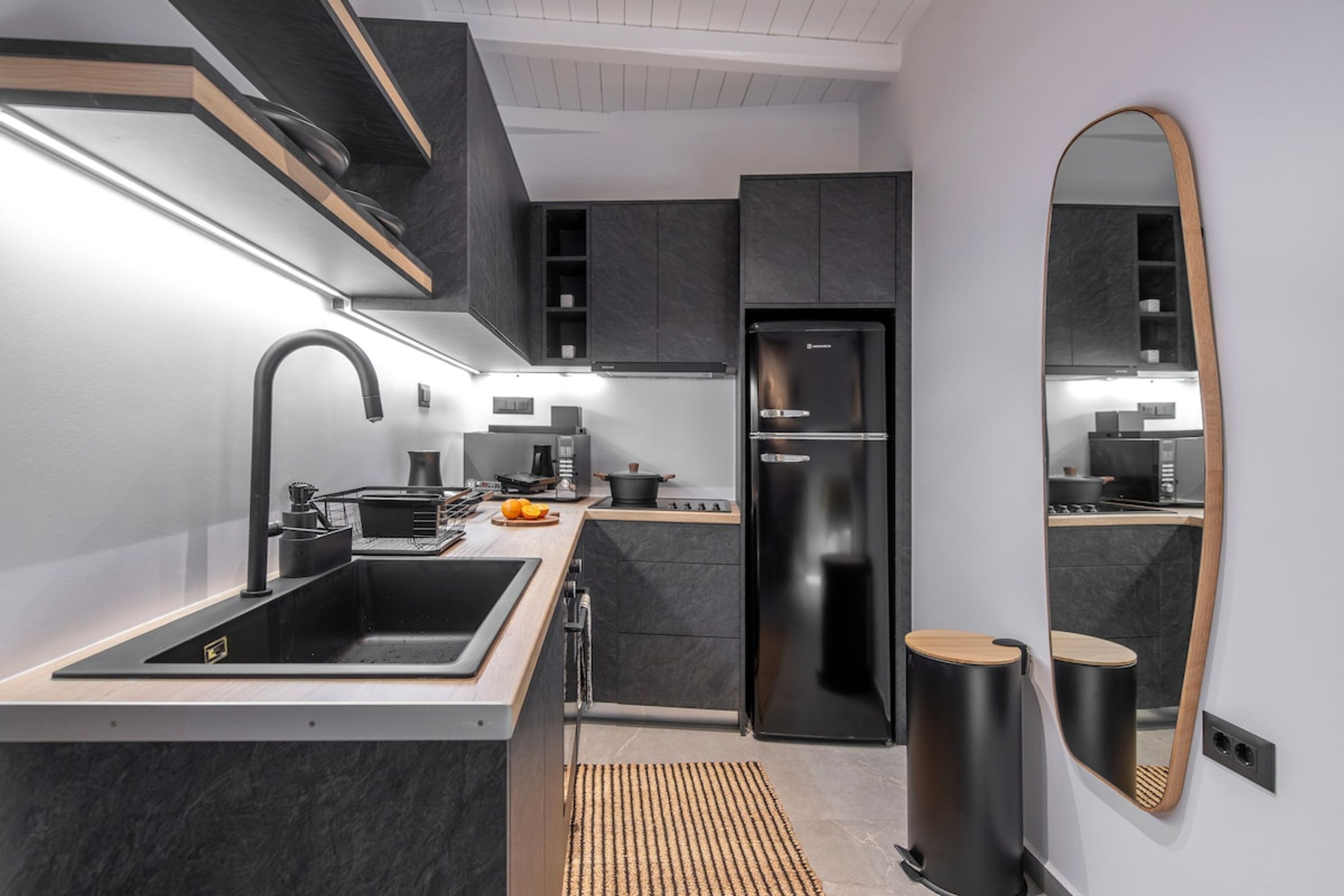 Una cocina moderna con armarios oscuros, un refrigerador negro y un espejo grande.