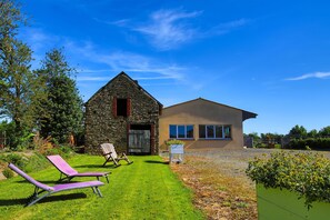 Un bâtiment en pierre doté d’une extension moderne, une pelouse verdoyante et deux fauteuils de jardin.