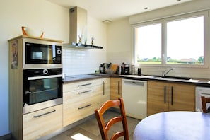 A modern kitchen with a double oven, a dishwasher, and a window with a view of the outdoors. - Holiday Home "Le Jardin" with Private Terrace and Wi-Fi (Lison)