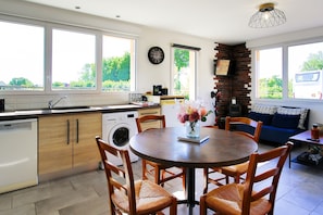 A modern kitchen with a dining area, large windows, and a brick accent wall. - Holiday Home "Le Jardin" with Private Terrace and Wi-Fi (Lison)