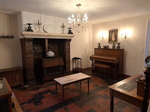A room with a fireplace, a piano, a table, and a chandelier.