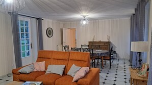 A living room with a sofa, a dining table, and a chandelier. - Gîte LEBASLADIN for 7 Guests – Renovated Holiday Home in Lison (Lison)