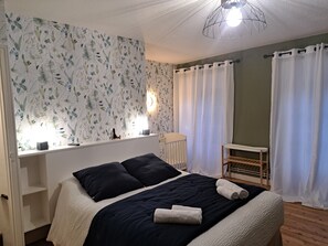 A bedroom with a bed, a nightstand, a crib, and a window with curtains.