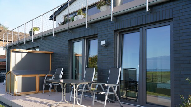A modern outdoor deck with a built-in grill, seating area, and large windows offering views of the surrounding landscape. - Passat - View of the river, terrace, garden, private parking space, fly screens (Olpenitzdorf)