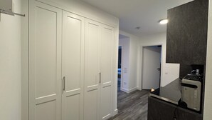 A hallway with a white wardrobe, a dark kitchen area with a stove, and a door leading to another room. - Pamir - View of the river, terrace, garden, induction stove, parking space (Olpenitzdorf)