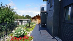 A pathway leading to a building with a stone planter with red and white flowers. - Pamir - View of the river, terrace, garden, induction stove, parking space (Olpenitzdorf)