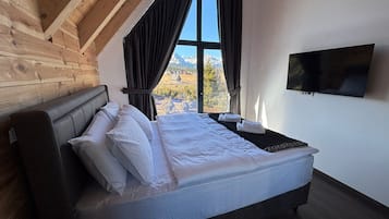 A bedroom with a bed, a TV, and a window with curtains.