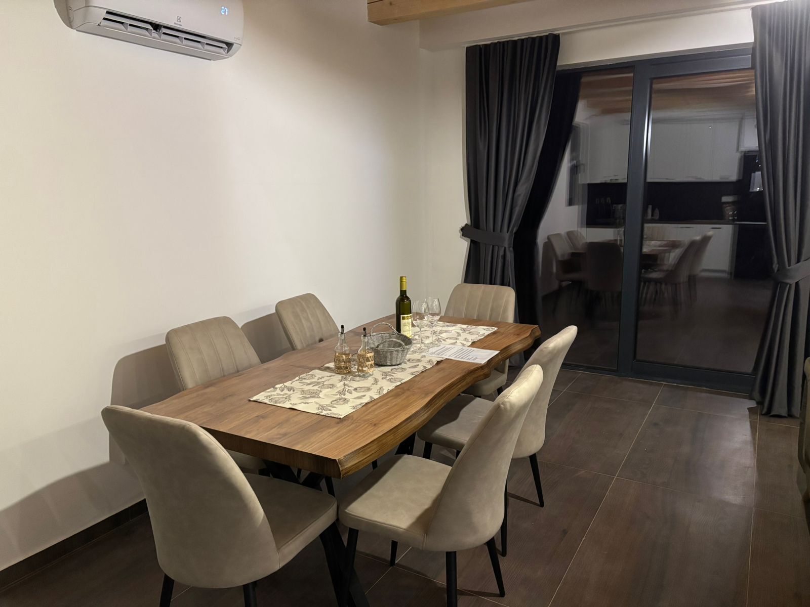 Zona pranzo con tavolo in legno, sei sedie e un divisorio in vetro.