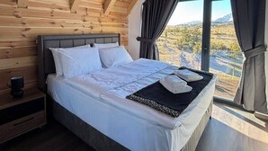 A bedroom with a wooden ceiling, a large bed, a nightstand, and a window with a view of a mountainous landscape. - Rustic Authentic House, chalet style,  in charming Žabljak. (ZABLIJAK)