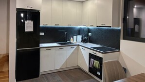 Una cocina compacta con un refrigerador negro, gabinetes blancos, una encimera negra y un horno empotrado.