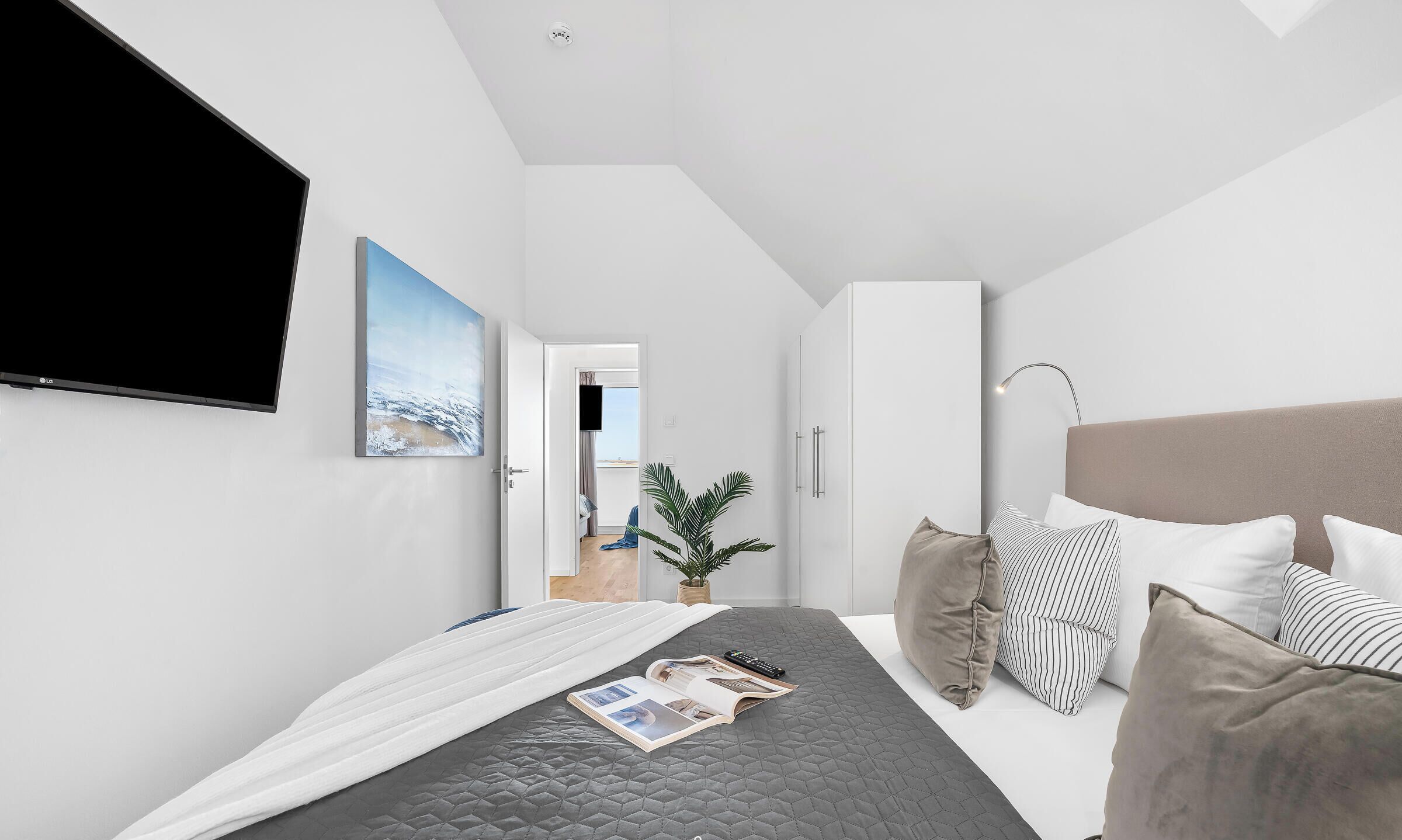 Een moderne slaapkamer met een bed, een televisie, een plant en uitzicht op buiten.