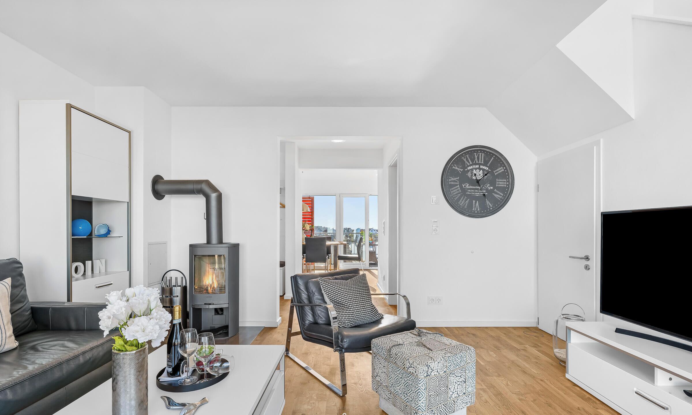 A modern living room with a fireplace, a dining area, and a large wall clock.