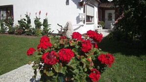 Une maison blanche avec une antenne parabolique, une boîte aux lettres et un jardin où poussent des fleurs rouges.