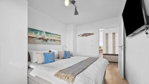 Un dormitorio moderno con una cama, un cuadro, una lámpara de techo y un televisor.