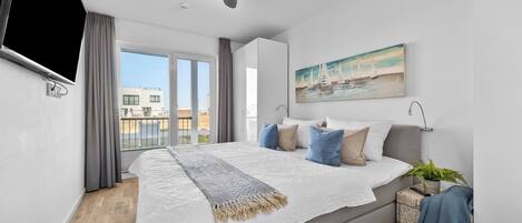 Ein modernes Schlafzimmer mit einem großen Bett, einem an der Wand montierten Fernseher und Blick auf die Stadt.