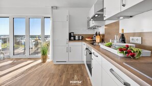 Cocina moderna con armarios blancos, electrodomésticos de acero inoxidable y encimera de madera. Una ventana grande ofrece vistas al exterior.