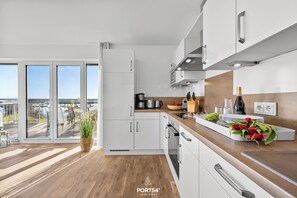 A modern kitchen with white cabinets, stainless steel appliances, and a wooden countertop. There is a large window providing a view of the outdoors. - Landungsbrücke 28 - 1st row on the waterfront, infrared cabin, whirlpool tub (Olpenitz)