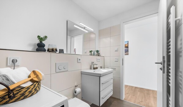 A modern bathroom with a white sink, mirror, and towel rack. - St. Tropez - 2nd Floor, Balcony, Harbor View, Private Parking, Washing Machine (Olpenitz)
