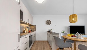 A modern kitchen with white cabinets, a wooden countertop, and a dining area with a table and chairs. - St. Tropez - 2nd Floor, Balcony, Harbor View, Private Parking, Washing Machine (Olpenitz)