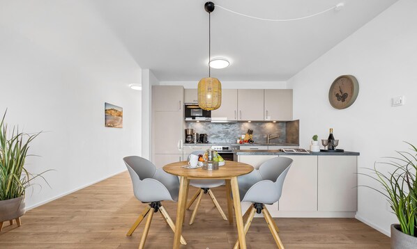 A modern kitchen with white cabinets, a round wooden table, and two grey chairs. - St. Tropez - 2nd Floor, Balcony, Harbor View, Private Parking, Washing Machine (Olpenitz)