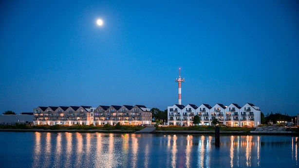 Un hotel frente al agua con edificios de varios pisos, un faro destacado y reflejos en el agua.